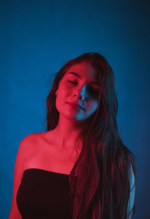 Slim, beautiful young girl in black top posing in neon red and blue light