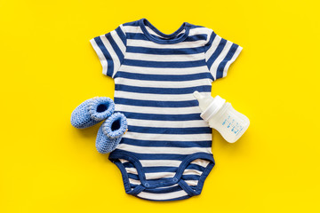 Blue bodysuit for baby boy near children's accessories on yellow background top-down