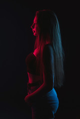 Slim, beautiful young girl in black top posing in neon red and blue light