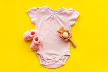 Pink bodysuit for baby girl near children's things on yellow background top-down