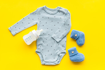 Cute baby clothes - suit - booties and accessories on yellow table top-down