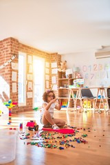 Beautiful toddler wearing glasses and unicorn diadem playing with tractor, building blocks toy and tennis racket at kindergarten