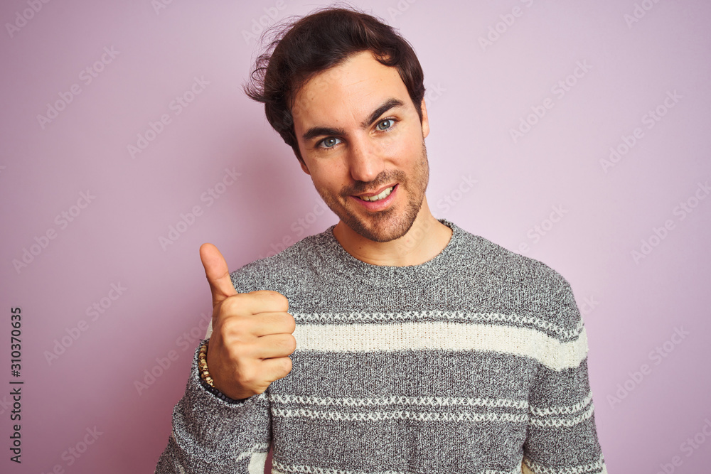 Sticker Young handsome man wearing casual striped sweater standing over isolated pink background happy with big smile doing ok sign, thumb up with fingers, excellent sign