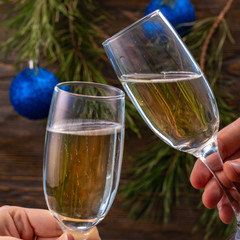 Glasses of champagne with bubbles on the background of Christmas decorations. Glasses in the hands of people touch during a festive toast. Beautiful card. Square.