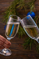 Glasses of champagne with bubbles on the background of Christmas decorations. Glasses in the hands of people touch during a festive toast. Beautiful card.