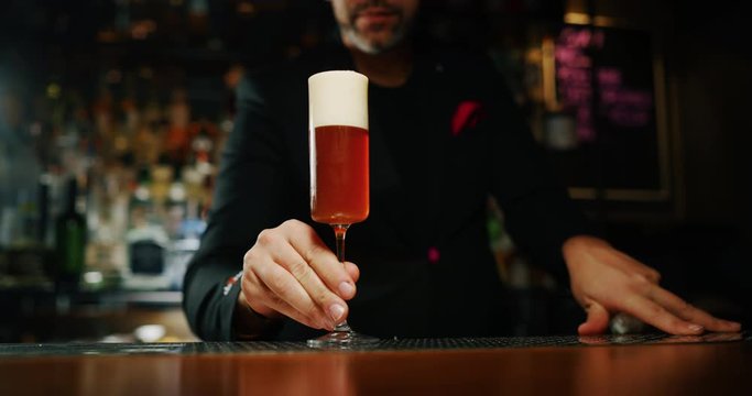 A professional bartender is serving an long drink cocktail to customers at the bar or disco club.