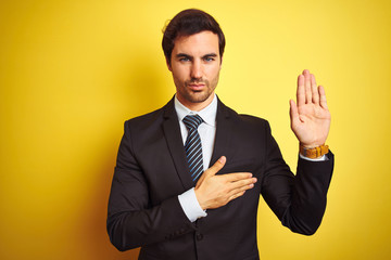 Young handsome businessman wearing suit and tie standing over isolated yellow background Swearing...