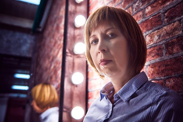 Girl in shirt in front of a lighted mirror in a dark room. Model posing for a photo shoot in the...