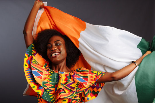 Happy african woman in national clothes smiling and posing with a flag Ivory Coast, C te d'Ivoire isolated over a gray background