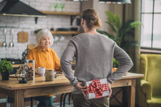 Tall Man In Grey Shirt Hiding A Present For Mom Behind His Back