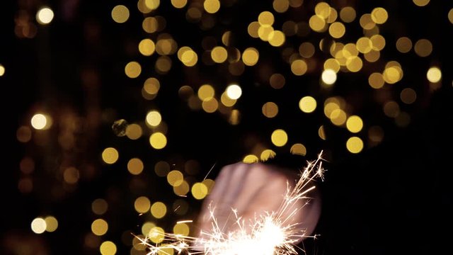 Merry Christmas. Sparkler flashes in hands on a black glare background close-up. The bright flame light of a burning bengal light and golden sparks flicker and fly apart. Magic bengali New Year.