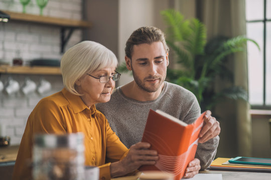 Elegant good-looking grey-haired woman and her son reading a book