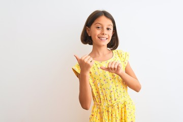 Young beautiful child girl wearing yellow floral dress standing over isolated white background Pointing to the back behind with hand and thumbs up, smiling confident