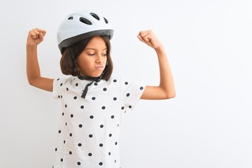 Beautiful child girl wearing security bike helmet standing over isolated white background showing arms muscles smiling proud. Fitness concept.