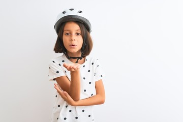 Beautiful child girl wearing security bike helmet standing over isolated white background looking at the camera blowing a kiss with hand on air being lovely and sexy. Love expression.