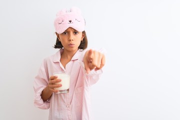 Child girl wearing sleep mask and pajama drinking glass of milk over isolated white background pointing with finger to the camera and to you, hand sign, positive and confident gesture from the front