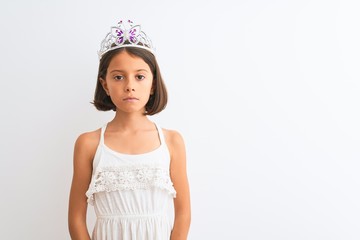 Beautiful child girl wearing princess crown standing over isolated white background Relaxed with serious expression on face. Simple and natural looking at the camera.