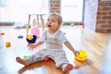 Adorable blonde toddler smiling happy playing around lots of toys at kindergarten