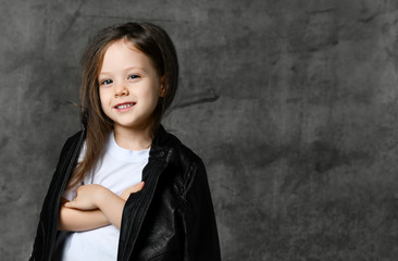 Small smiling cute girl in black and white rock star style casual clothing and white sneakers standing over grey concrete background