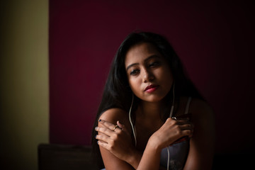 An young and attractive Indian Bengali brunette woman in white sleeping wear listening music sitting on a bed inside in her room. Indian lifestyle.