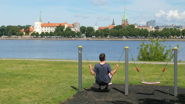man swinging on swing, watching riga view, latvia