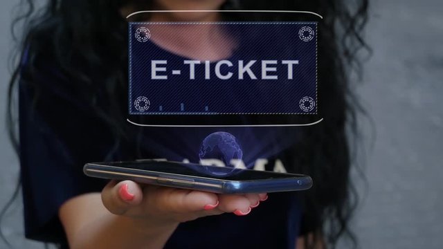 Unrecognizable curly brunette woman showing HUD hologram with text E-ticket. Girl uses technology of the future on a mobile screen