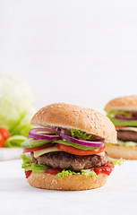 Big sandwich - hamburger burger with beef, avocado, tomato and red onions on light background. American cuisine. Fast Food