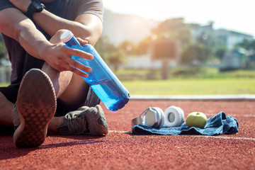 Man runner is holding bottle of water. Tired man is drinking water after run exercise.