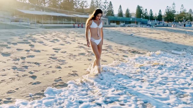 Reverse shot of an attractive girl in a bikini walking on wet sand at a beach