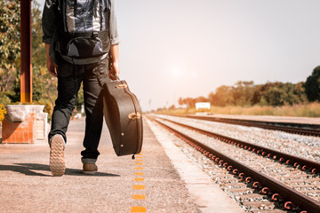 Backpacker is holding guitar case at railway station. - Powered by Adobe