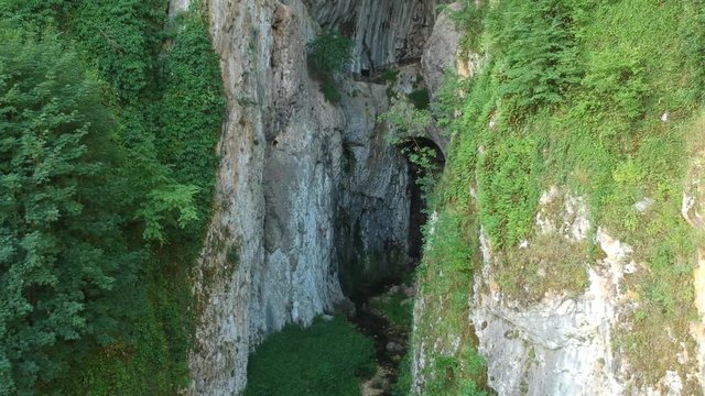 Beautiful secluded monumental entrance in the Potpec cave, shaped like a horseshoe, Cliff of Dreznicka Gradina Mountain, aerial, drone dolly out establishing shot