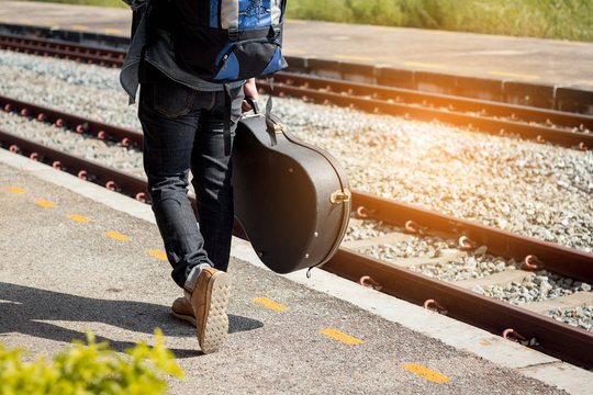 Backpacker Is Holding Guitar Case At Railway Station.