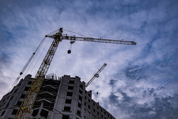 Fototapeta premium Tower cranes and unfinished multi-storey high buildings under construction site in the evening with dramatic colorful cloud background