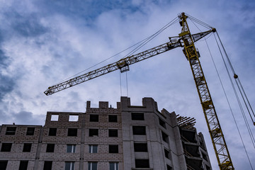 Tower cranes and unfinished multi-storey high buildings under construction site in the evening with dramatic colorful cloud background