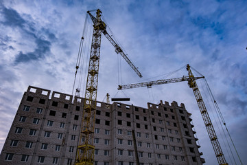 Tower cranes and unfinished multi-storey high buildings under construction site in the evening with dramatic colorful cloud background