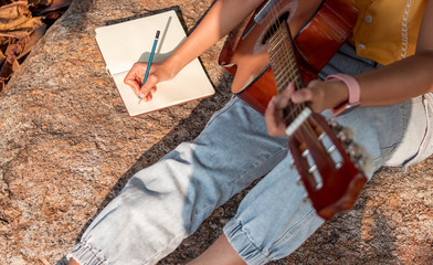 Songwriter writing on notebook with acoustic guitar.
