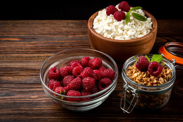 Cottage cheese, granola and fresh raspberry on dark wooden background.