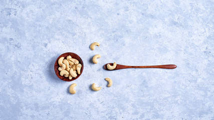 cashew nut in a wooden bowl whith wooden spoon on a blue and white background top view