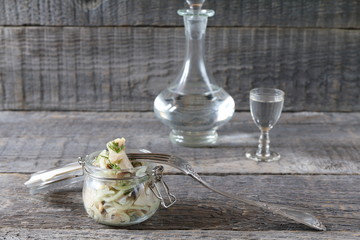 Jar of salted herring on the background of a glass of vodka and decanter. Salted herring in jar as...