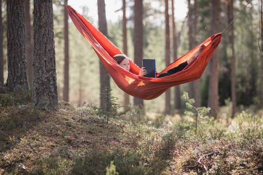 Teenage girl reading book in hammock in forest