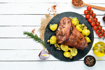 Baked pork leg with potatoes on a black stone plate. Pepper steak. Top view, free space for your...