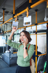 Young adorable joyful woman is standing on the bus using the phone and smiling.