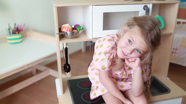 Cute little girl sits on toy kitchen