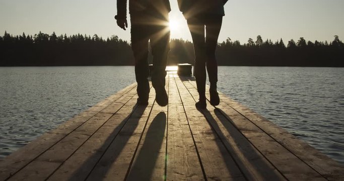 Silhouette of man and woman couple walking on wooden jetty