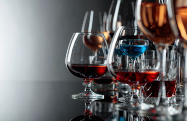 Set of various alcoholic beverages in glasses on a black reflective background.