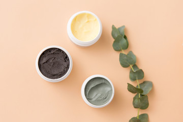 beauty, spa and wellness concept - blue clay mask, body butter, therapeutic mud and eucalyptus cinerea on beige background