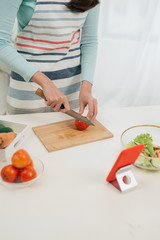 The young happy woman in apron looking at recipe in tablet in the kitchen. Vegetable salad. Dieting concept. Healthy lifestyle. Cooking at home. Prepare food.