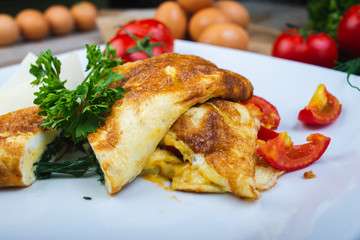 Traditional omelet with vegetables, spinach, tomatoes and herbs on a wooden table in a restaurant.