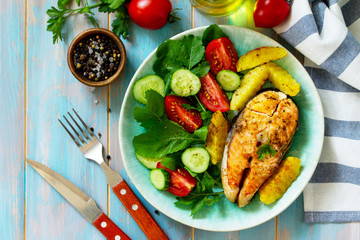 Dietary and healthy nutrition. Grilled salmon steak and baked potatoes with fresh vegetable salad on a wooden table. Top view on a flat background.