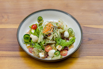 Greek salad is served on special plate on the wooden table.